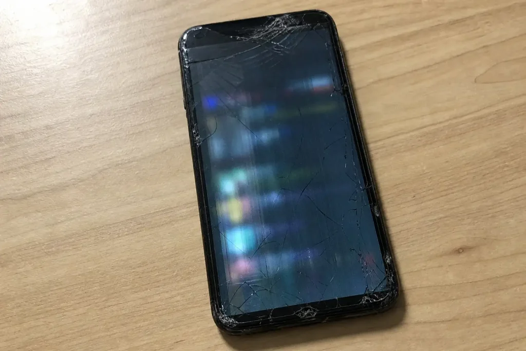 En sliten smartphone med sprucken skärm på ett träbord, ett vanligt exempel på hur länge en mobiltelefon kan hålla.