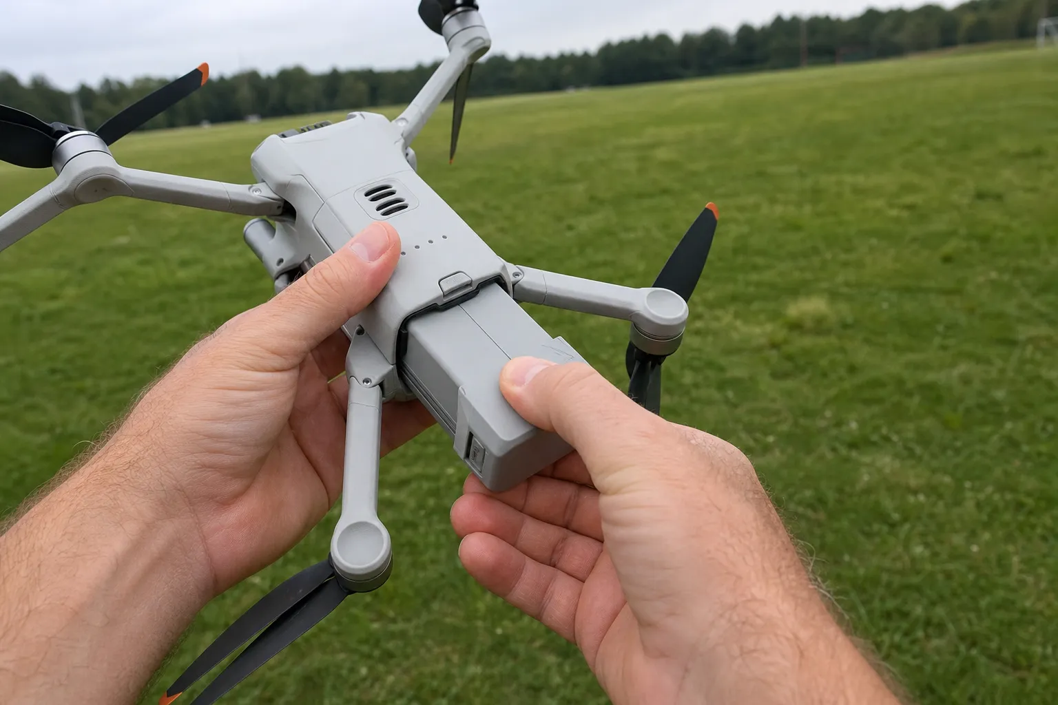 Händer sätter i batteriet på en självflygande drönare utomhus vid en gräsäng