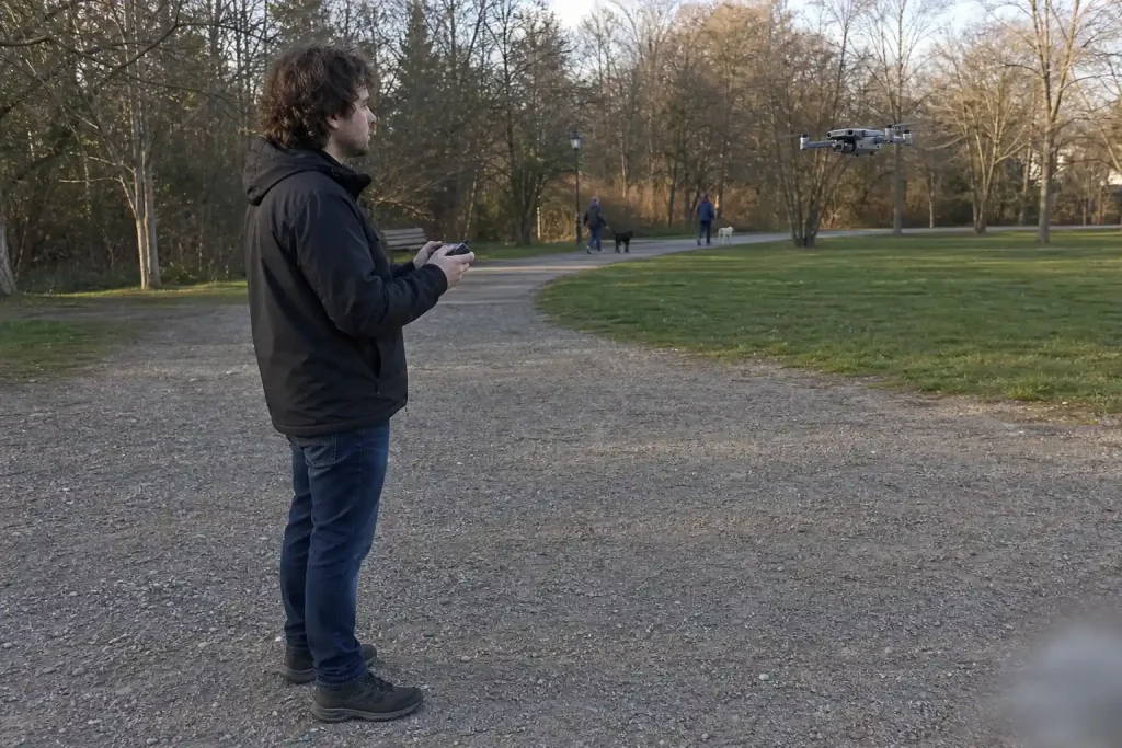 En person styr en HoverAir VERSA drönare som svävar i luften på en grusgång i en park.
