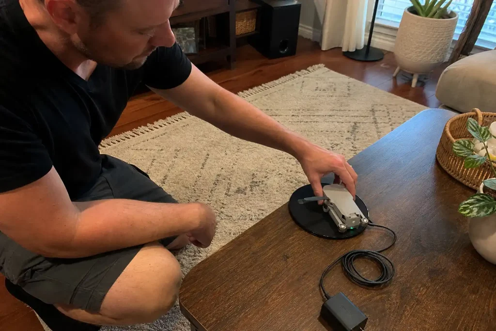 Drönare med lipo batteri laddas på trådlös laddplatta i vardagsrummet medan en person justerar den.
