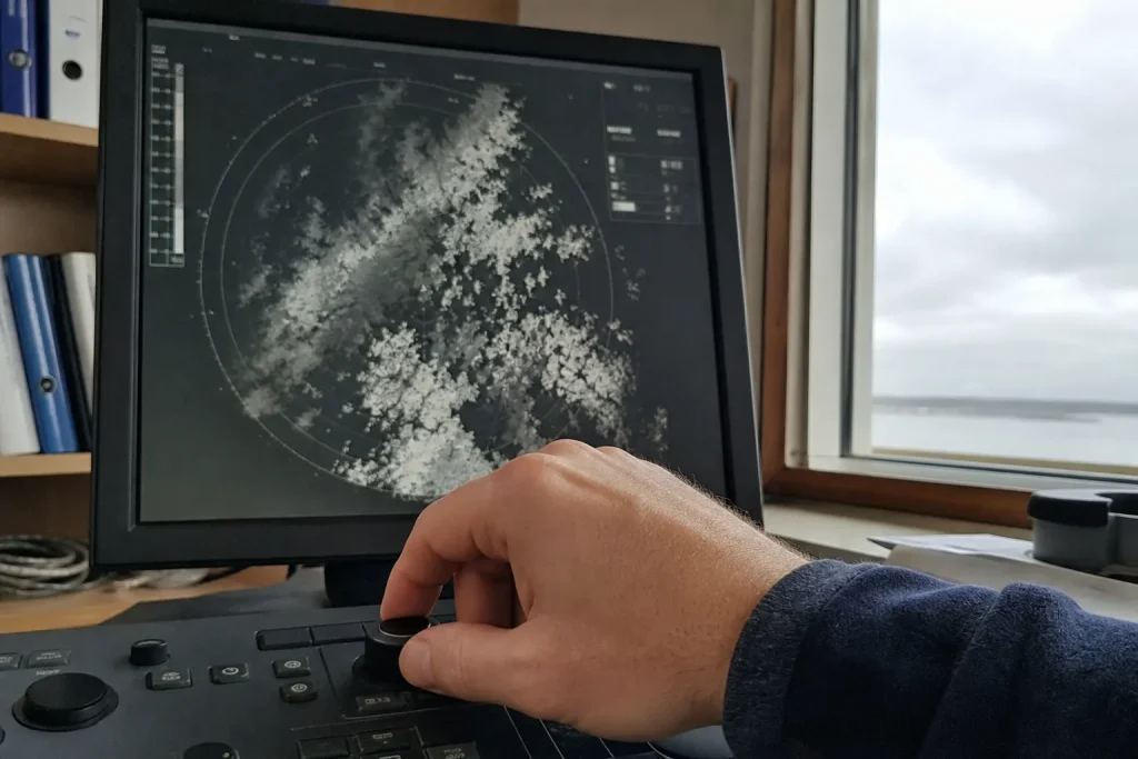 En hand justerar en väderradarmonitor med gråskaliga molnmönster, kopplat till att Sveriges första satellitbilder är här.